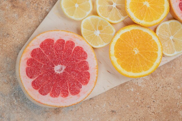 Tranches de citron, orange et pamplemousse sur planche de bois.