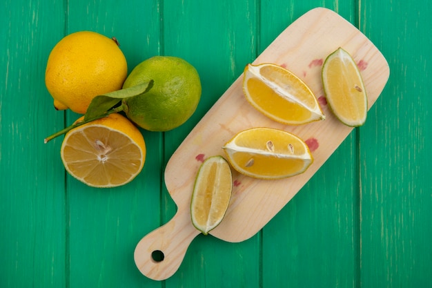 Photo gratuite tranches de citron vert vue de dessus avec des citrons sur une planche à découper sur fond vert