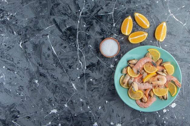 Tranches de citrons et de crevettes sur une assiette à côté d'un bol de sel, sur fond de marbre.