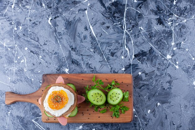 Tranches de concombre et sandwich sur une planche à découper, sur le fond bleu.