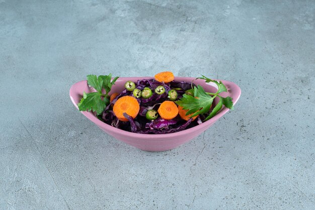 Tranches de divers légumes et verts dans un bol rose.