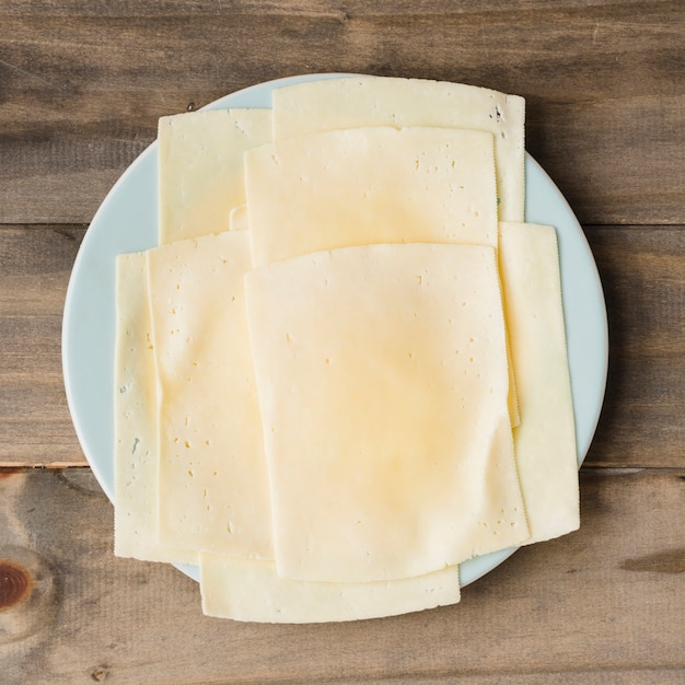 Tranches de fromage sur une plaque blanche sur fond de planche de bois
