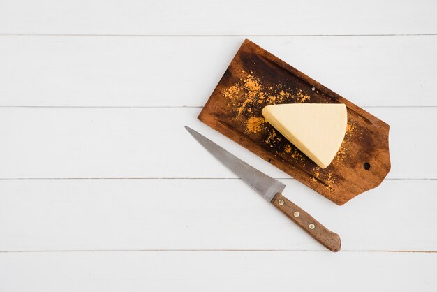 Tranches de fromage saupoudrées d&#39;épices sur une planche à découper avec un couteau tranchant sur la table blanche