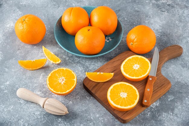 Tranches de fruits orange avec des oranges entières sur une planche de bois.