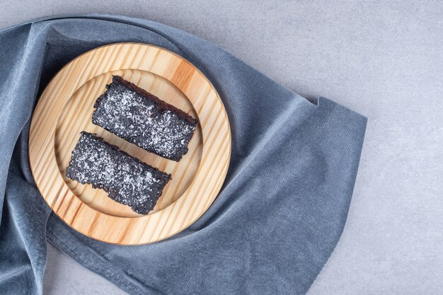 Tranches de gâteau au chocolat sur un plateau en bois sur une serviette sur une table en marbre.