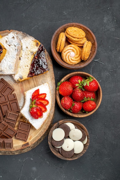 Tranches de gâteau vue de dessus avec des biscuits aux fruits et des barres de chocolat sur un bureau sombre