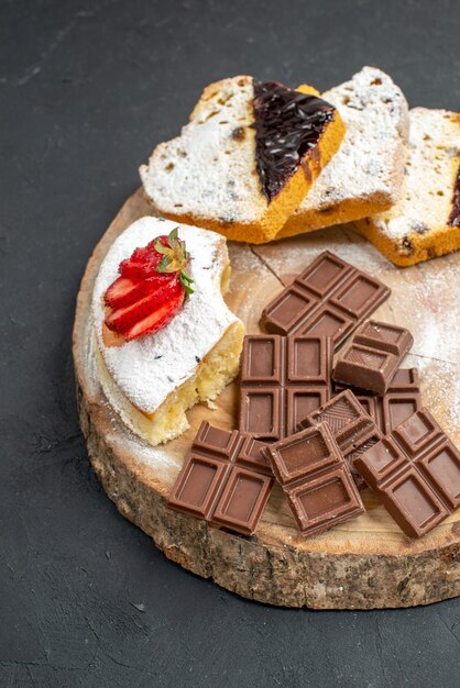 Tranches de gâteau vue de face avec des barres de chocolat sur fond sombre