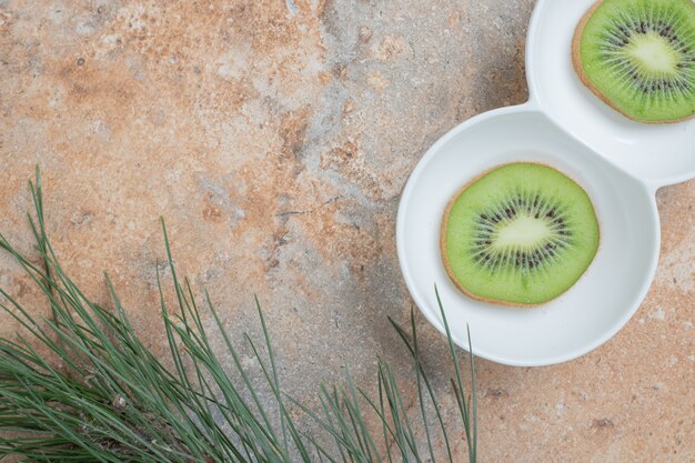 Tranches de kiwi frais sur plaque blanche.