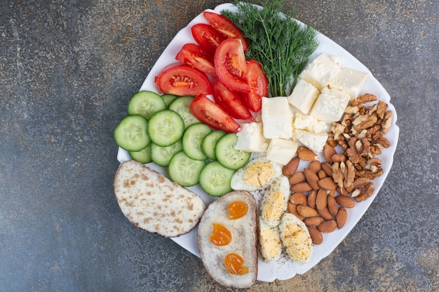 Tranches de légumes, œufs, fromage et noix sur plaque blanche.