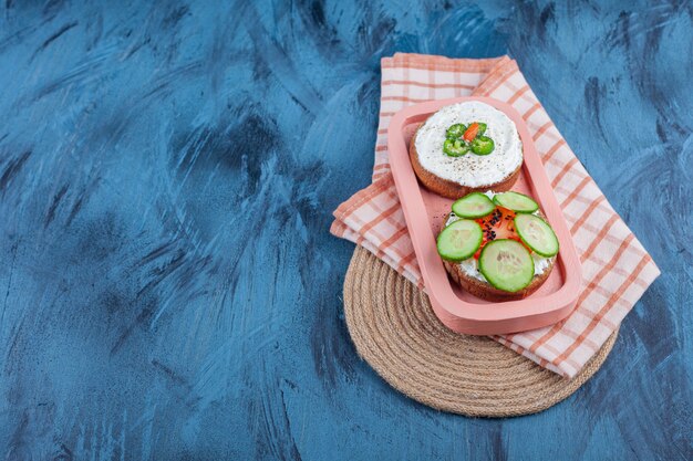 Tranches de légumes sur pains au fromage à bord sur une serviette sur un dessous de plat sur bleu.