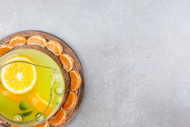 Tranches de mandarine autour de limonade d'agrumes frais sur plateau en bois sur table grise.