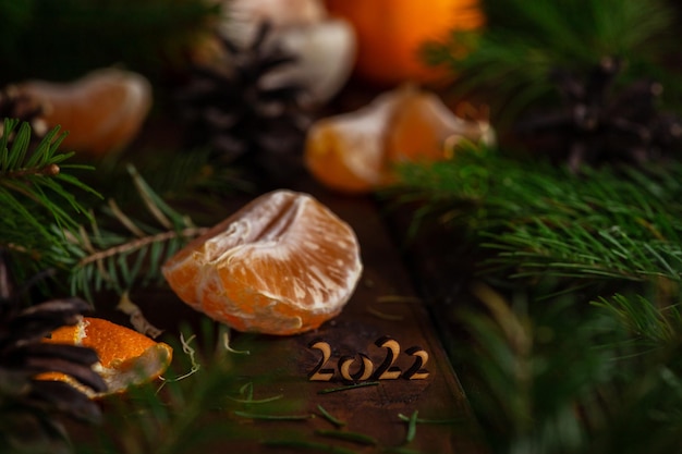 Des tranches de mandarine reposent sur une table en bois entourée de brindilles d'épinette verte. il y a des numéros 2022 en bois à côté