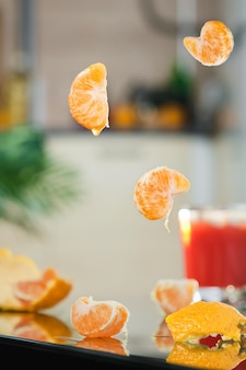 Tranches de mandarine volantes sur le fond de la cuisine, pelure et feuilles sur une table en miroir. mise au point sélective sur les tranches de fruits en lévitation. l'idée de faire un cocktail ou un jus de mandarine