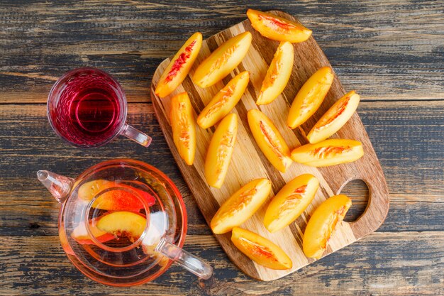 Tranches de nectarine avec boisson sur table en bois et planche à découper, pose à plat.