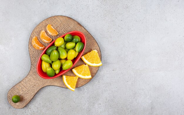 Tranches d'orange et de mandarine avec bol de kumquats sur planche de bois.