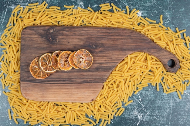 Tranches d'orange sur planche de bois avec tas de pâtes crues. Photo de haute qualité