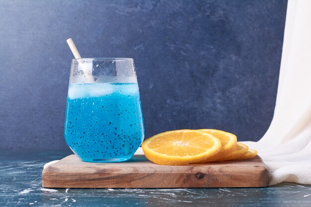 Tranches d'orange avec une tasse de boisson sur bleu.