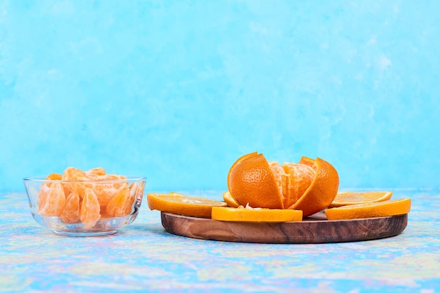 Tranches d'oranges et de mandarines isolées sur un plateau en bois et dans une tasse en verre sur fond bleu. Photo de haute qualité