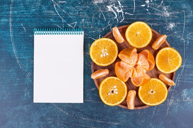 Tranches d'oranges et de mandarines sur un plateau en bois avec un cahier de côté. Photo de haute qualité