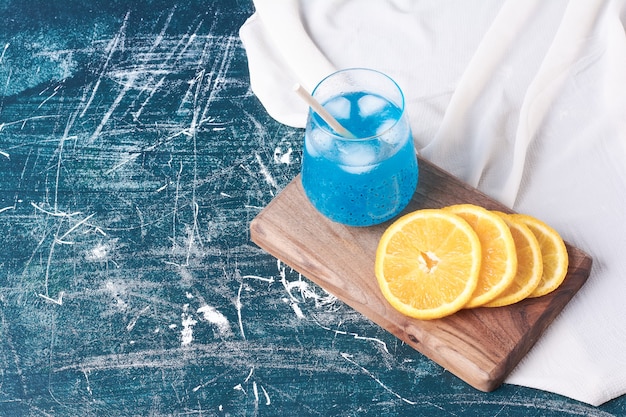 Tranches d'oranges avec une tasse de boisson sur bleu.