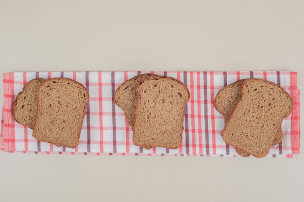 Tranches de pain brun frais sur nappe