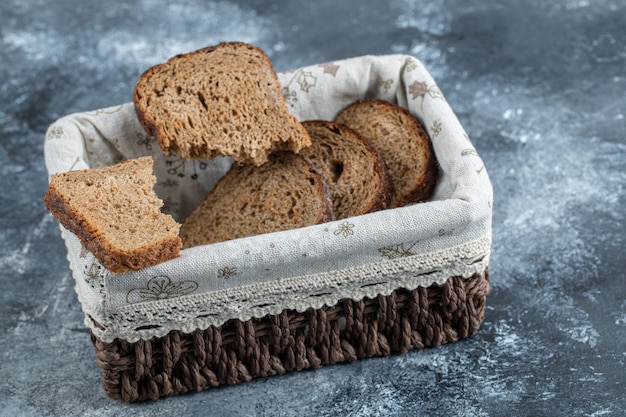 Tranches de pain brun sur un panier sur une surface grise.