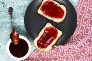 Photo gratuite tranches de pain avec de la confiture de fraises dans une assiette grise et une tasse de confiture.