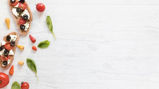 Tranches de pain garnies de tomates; fromage et olives sur table blanche