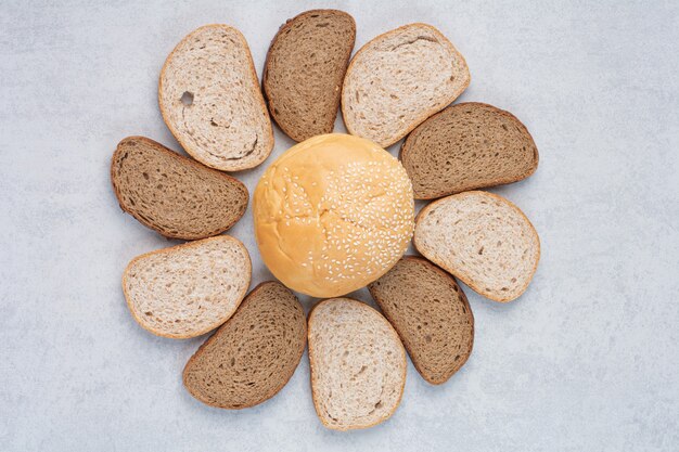 Tranches de pain et petit pain aux graines de sésame sur une surface bleue