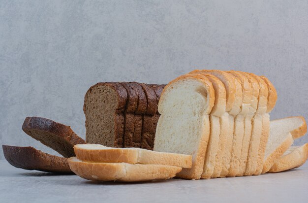 Tranches de pains frais blancs et bruns sur fond de marbre.