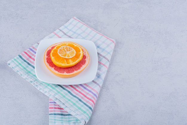 Tranches de pamplemousse frais, orange et citron sur plaque blanche.