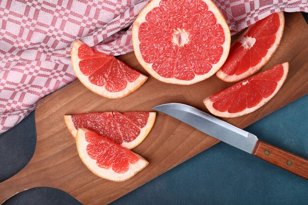 Tranches de pamplemousse frais rouge sur une planche de bois avec un couteau.