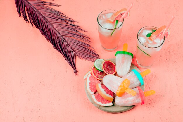 Tranches de pamplemousse; jus et sucettes glacées à la feuille sur fond de corail texturé
