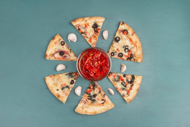 Tranches de pizza et bol de poivrons rouges marinés sur table bleue.