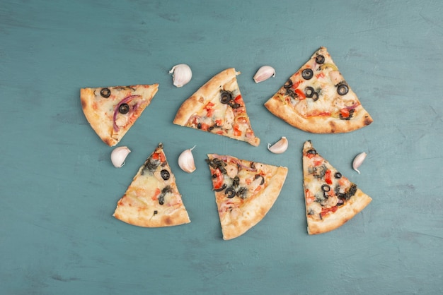 Tranches de pizza et morceaux d'ail sur une surface bleue.
