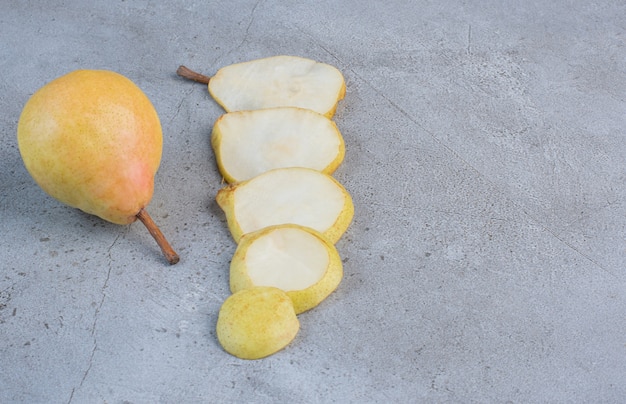 Photo gratuite tranches de poire alignées à côté d'une poire entière sur fond de marbre.