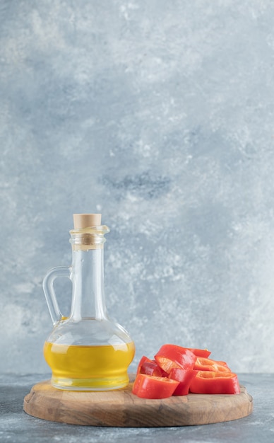 Tranches de poivron rouge doux avec une bouteille en verre d'huile sur planche de bois.