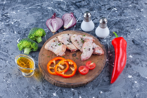 Tranches de poivron, tomates et aile sur une planche à côté de l'oignon, sel et poivre sur la surface bleue