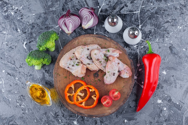 Tranches de poivron, tomates et aile sur une planche à côté de l'oignon, sel et poivre sur la surface bleue