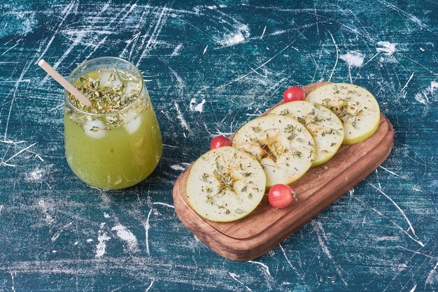 Tranches de pomme avec une tasse de boisson sur bleu.