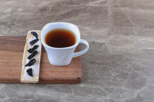 Tranches de prune sèche sur le pain croustillant et tasse de thé sur la planche de bois, sur la surface en marbre