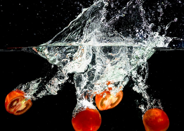Tranches de tomates tombant dans les éclaboussures d&#39;eau sur fond noir