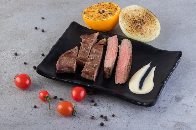 Tranches de viande fraîche avec des légumes frais placés sur une table en pierre.