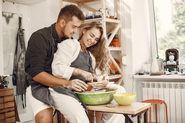 Travail créatif mutuel. Jeune beau couple en vêtements décontractés et tabliers. Les gens créant un bol sur un tour de poterie dans un studio d'argile.