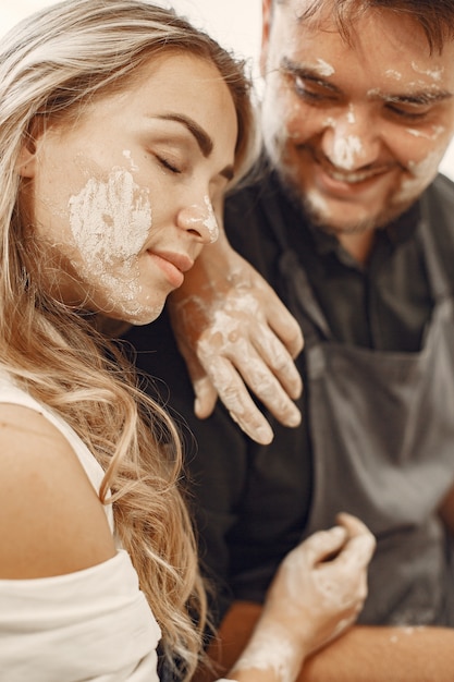 Travail créatif mutuel. Jeune beau couple en vêtements décontractés et tabliers. Les gens créant un bol sur un tour de poterie dans un studio d'argile.