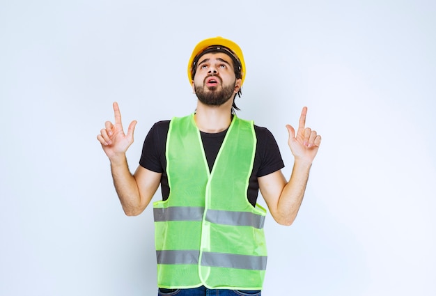 Photo gratuite travailleur en casque jaune et veste verte pointant vers le haut.