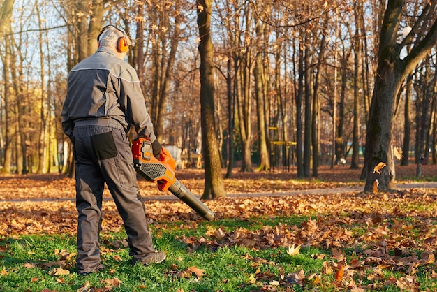 Photo gratuite travailleur à cheveux gris utilisant un souffleur de feuilles dans un parc de la ville en octobre vue arrière d'un homme âgé concentré