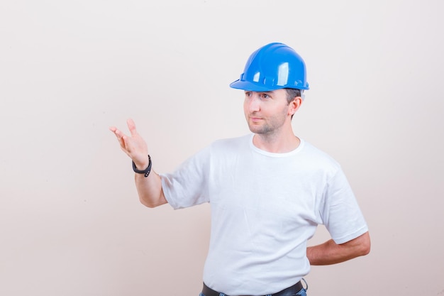 Travailleur de la construction gardant la main en question en t-shirt, jeans, casque et à la recherche de joie