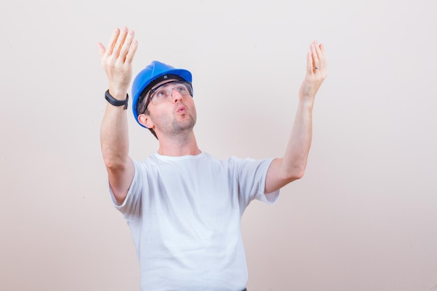 Photo gratuite travailleur de la construction levant les mains en levant les yeux en t-shirt, casque et l'air surpris
