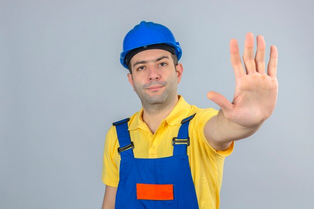 Travailleur de la construction en uniforme et bleu casque de sécurité faisant un geste d'arrêt avec la main isolé sur blanc